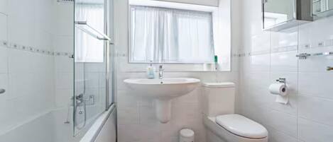 A modern bathroom with a glass shower enclosure, a sink, a toilet, and a window with curtains.