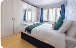 A bedroom with a bed, a wardrobe, and a window with curtains. - Modern Holiday Home 3bed (Basildon)