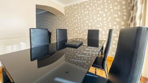 Une salle de conférence avec une table en verre et des chaises noires, un papier peint à motifs et une fenêtre avec des rideaux.