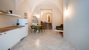 Una cocina moderna con armarios blancos, una zona de comedor con sillas verdes y una escalera que lleva a un dormitorio.
