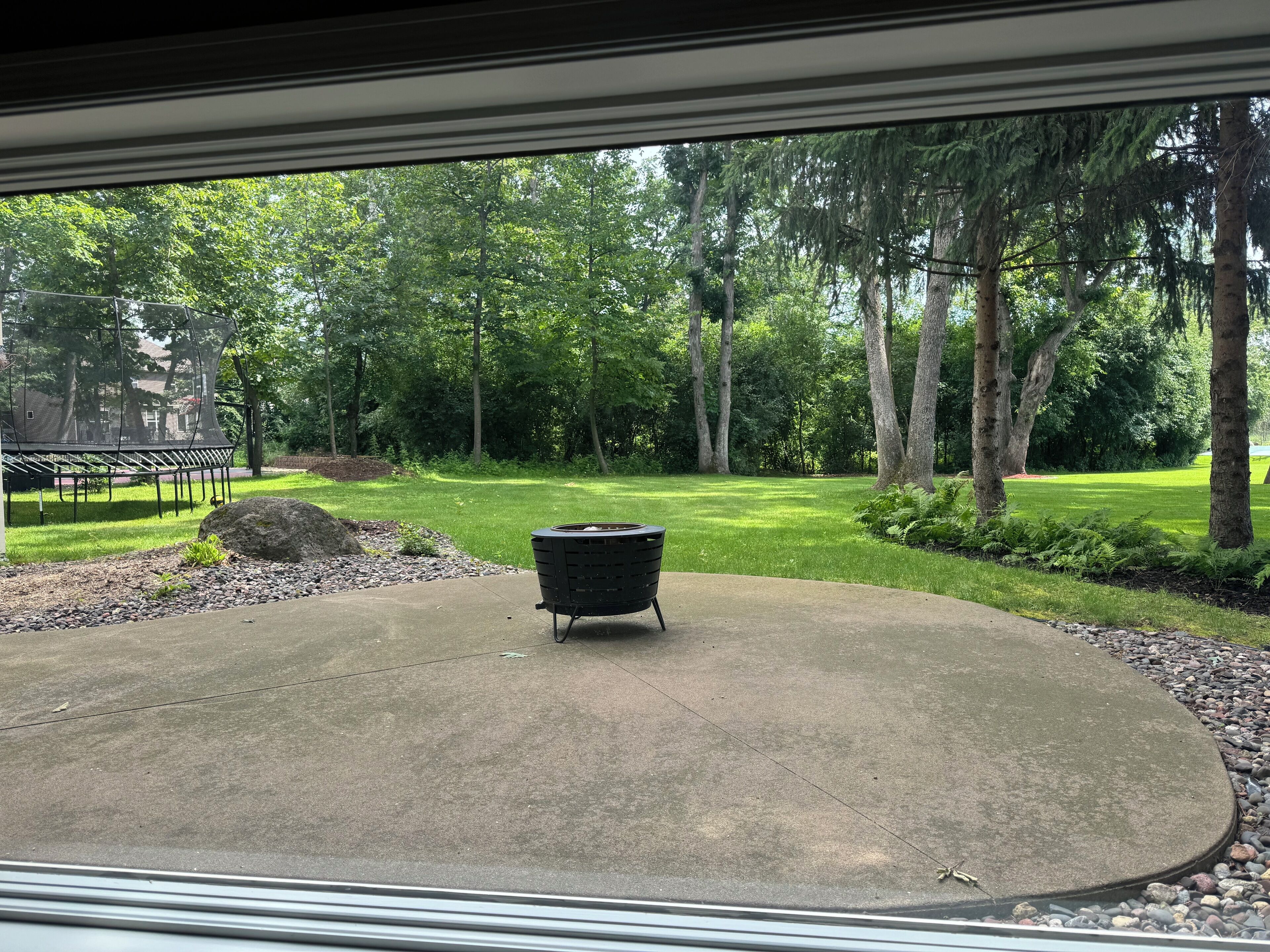 A patio with a fire pit, surrounded by a lawn and trees.