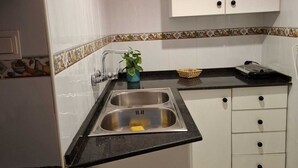 A compact kitchen with white cabinets, a black countertop, and a stainless steel sink.