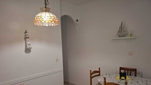 A dining area with a round table, wooden chairs, a hanging light fixture, and a small shelf with a model ship.