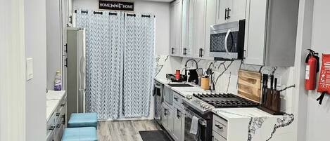 A modern kitchen with white cabinets, a stainless steel stove, and a microwave. There is a blue bench and a fire extinguisher mounted on the wall.
