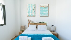 Habitación de hotel con una cama grande, dos obras de arte colgadas en la pared, una mesita de noche con lámpara y una ventana.