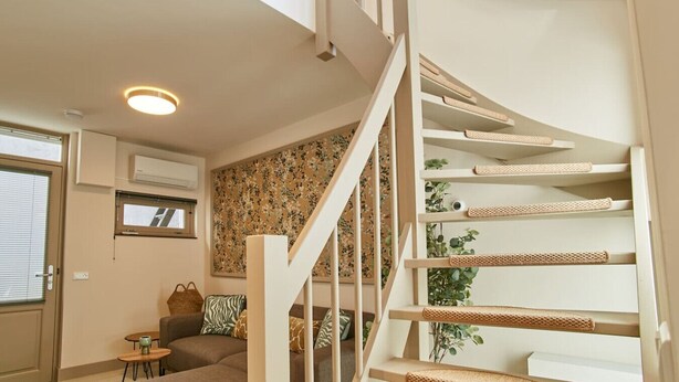 Een modern interieur met een spiltrap, een bank, een klein tafeltje en een raam met zonwering.