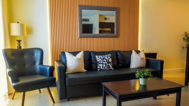 A living room with a black leather sofa, a matching armchair, a wooden accent wall, a mirror, and a coffee table with a plant.