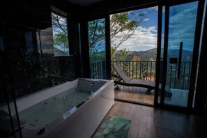 A modern bathroom with a large bathtub, a glass-enclosed shower area, and a balcony with a view of the mountains. - La Colina resort (La Vega)