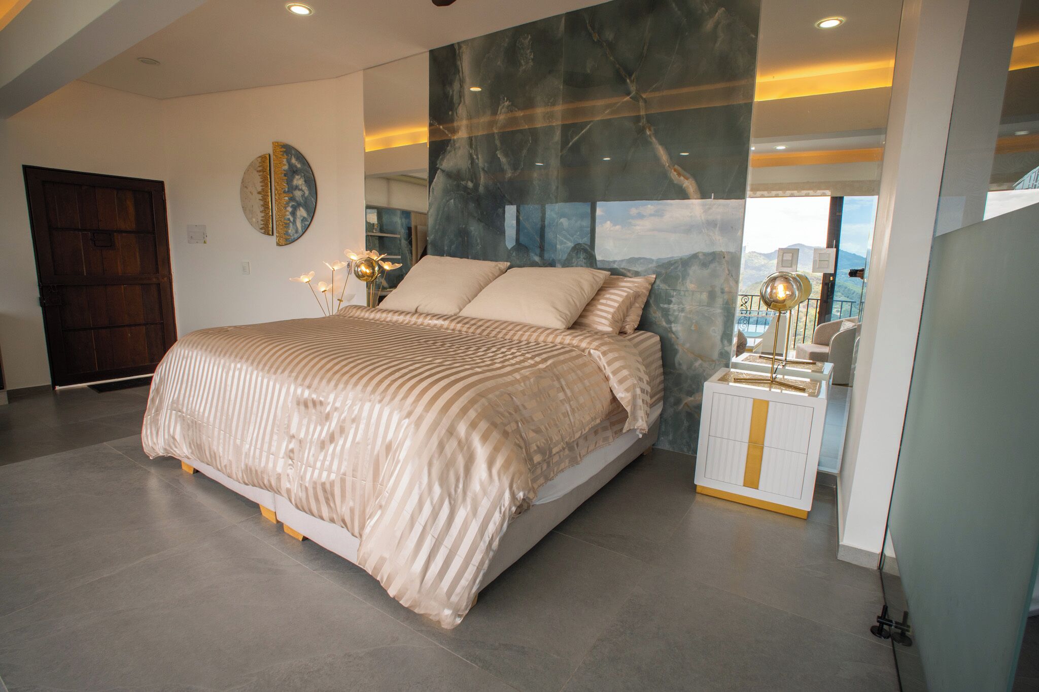 A modern bedroom with a large bed, a nightstand, and a view of the outdoors.