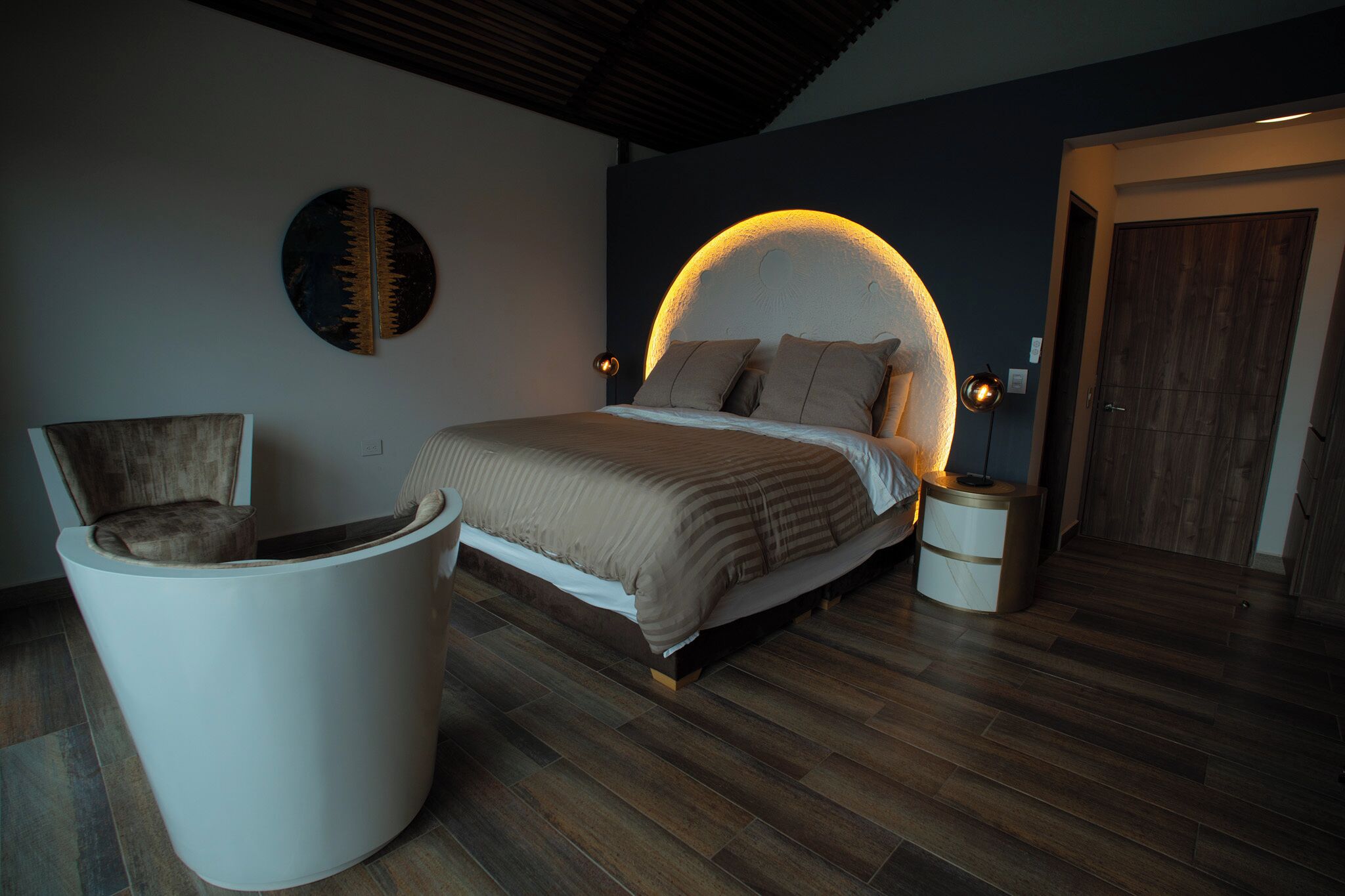 A bedroom with a bed, a chair, a round seating area, and a door.