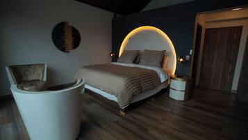A bedroom with a bed, a chair, a round seating area, and a door.