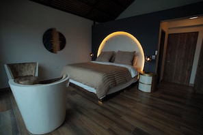 A bedroom with a bed, a chair, a round seating area, and a door. - La Colina resort (La Vega)