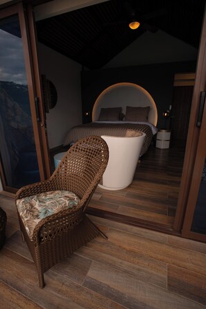 A room with a bed, a wicker chair, and a view of the outdoors. - La Colina resort (La Vega)