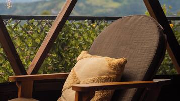 Una silla de madera con cojín, ubicada cerca de una ventana con vista a las montañas.