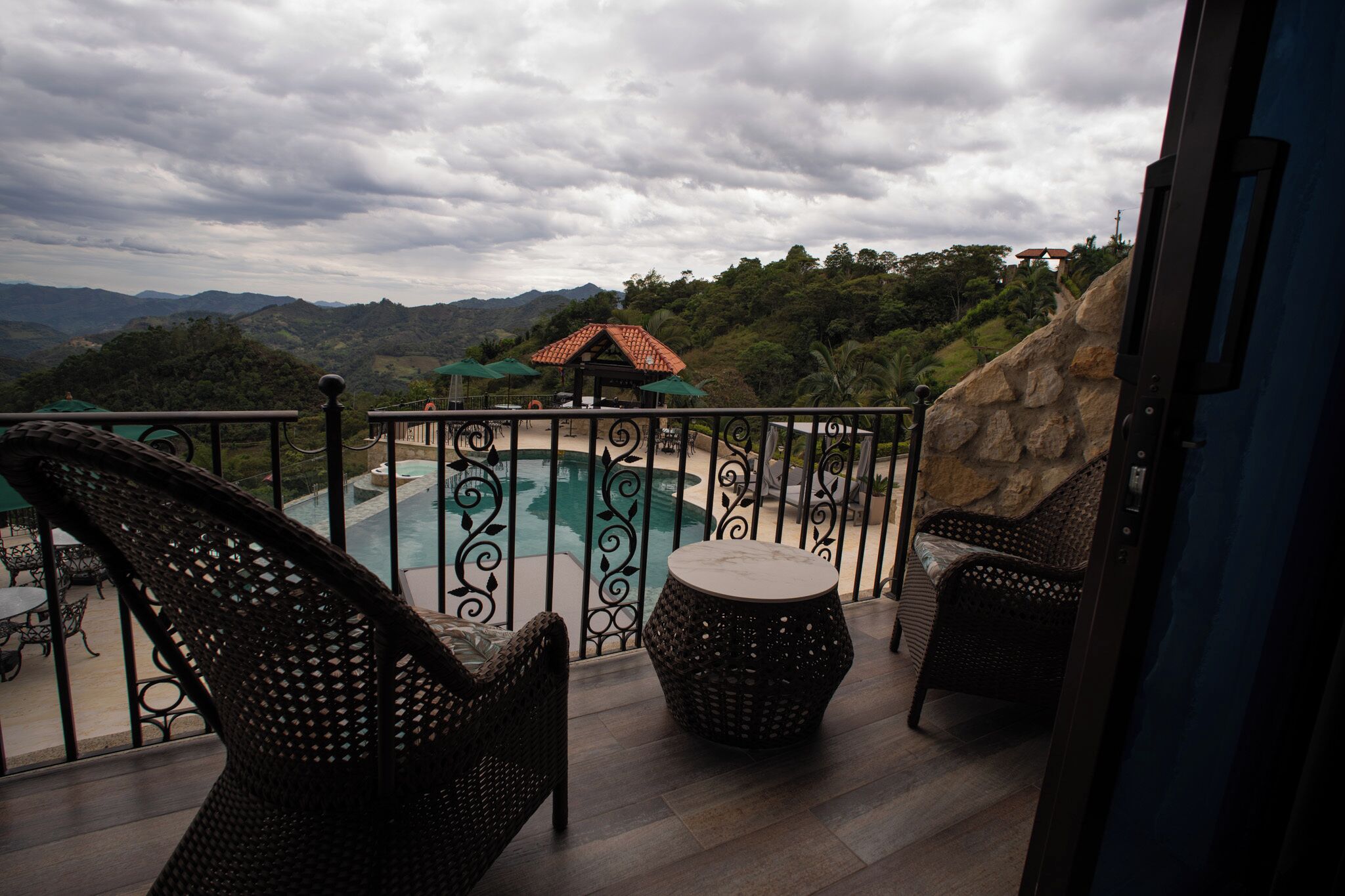 A balcony with a pool, wicker furniture, and a view of the mountains.