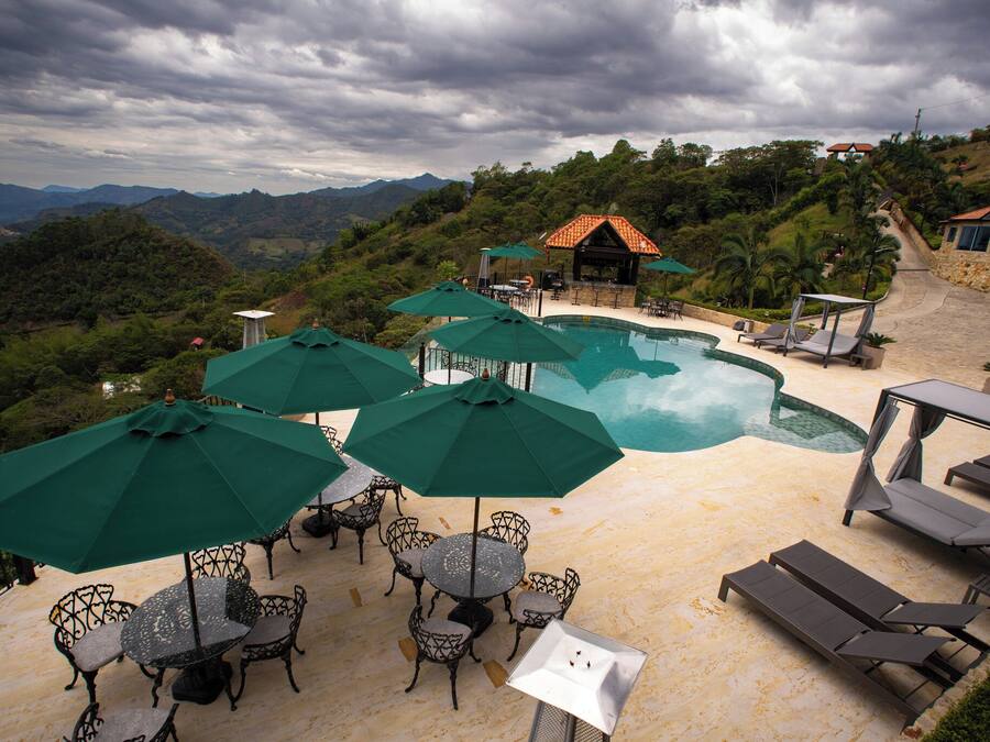 A poolside area with lounge chairs and umbrellas, surrounded by a mountainous landscape.