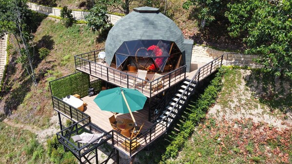 A modern, dome-shaped building with a wooden deck and outdoor seating area. - La Colina resort (La Vega)