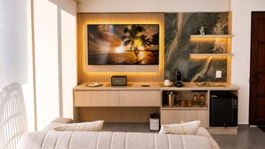 Et moderne hotelværelse med en seng, et skrivebord med en computer, en kaffemaskine og et maleri af en solnedgang.
