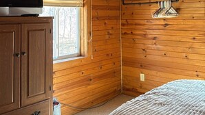 A cabin room with wooden walls, a window, a television on a cabinet, and a bed with a green skirt.
