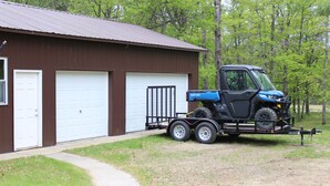 A blue utility vehicle with a trailer parked in front of a brown building with two white garage doors.