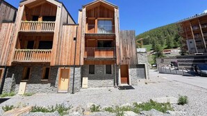 A wooden multi-story building with balconies, stone walls, and a clear sky. - Terrace, balcony, fireplace or stove, tv, 115m², Vars (Vars)