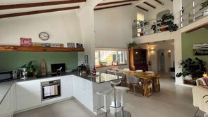Une cuisine spacieuse dotée d’un îlot central, un coin repas avec une table en bois et des tabourets de bar, et un loft avec un balcon offrant une vue sur la ville.