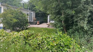 Asuinrakennus, jossa on patio, pieni varasto ja puutarha, jossa kasvaa monenlaisia kasveja ja kukkia.