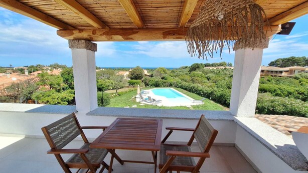 A covered patio with a wooden table and chairs, overlooking a swimming pool and lush greenery. - Villa with pool Porto Ottiolu (Porto Ottiolu)