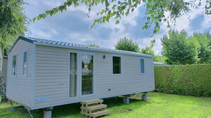 A single-story mobile home with a front door, two windows, and a small porch area. - Vakantiepark Klein Strand - Luxe Chalet 4p (Jabbeke)