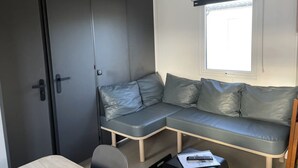 Ein gemütlicher Raum mit grauem Sofa, kleinem Tisch und einem Fenster mit Jalousien.