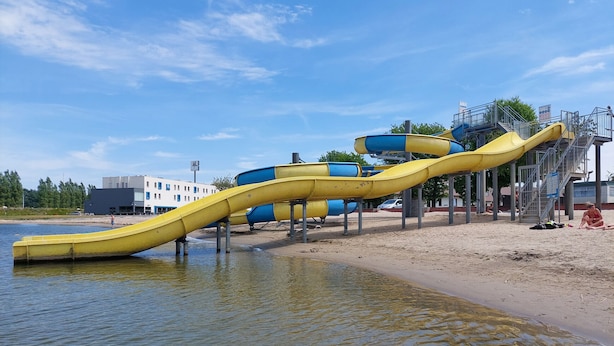 Estructura de tobogán acuático con toboganes amarillos y azules que se deslizan hacia una masa de agua, sostenida por postes metálicos.
