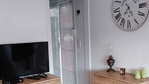 Una sala de estar con una televisión de pantalla plana sobre un mueble de madera, un reloj antiguo en la pared y una puerta que da a otra habitación.