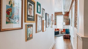 Um corredor com obras de arte emolduradas nas paredes, parede de tijolos e piso de madeira.