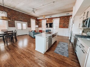 Una cocina amplia con una isla central, muebles blancos y una pared de ladrillo decorativa.