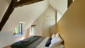 A bedroom with a sloped ceiling, a bed with pillows, a window, and a view of greenery outside. - Charming house in the heart of nature-Authentic Perche (Cour-Maugis sur Huisne)