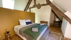 Ein Schlafzimmer mit Holzboden, einem Bett mit grüner Decke, einem kleinen Nachttisch und einem Holzstuhl.