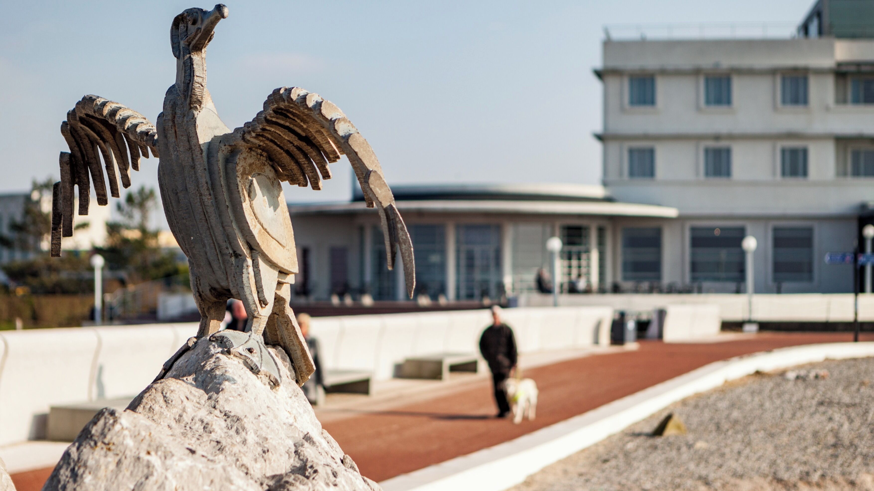 Eine Steinskulptur eines Vogels auf einem Felsen, im Hintergrund ein Gebäude.
