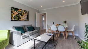 A modern living room with a grey sofa, a coffee table, and a dining area with a white table and chairs. - Altham Place-fully Refurbished 2-bath Bungalow (Morecambe)