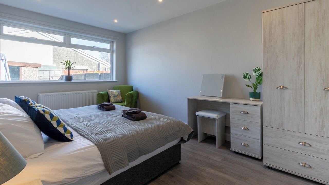 A bedroom with a bed, a desk, a wardrobe, and a window.