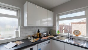 A modern kitchen with white cabinets, a black countertop, and a window with a view of a brick wall. - Altham Place-fully Refurbished 2-bath Bungalow (Morecambe)