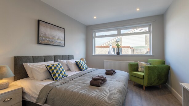 A modern bedroom with a large bed, a green armchair, a window with a view, and a radiator. - Altham Place-fully Refurbished 2-bath Bungalow (Morecambe)