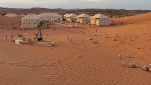 A desert landscape with several tents and a large building, likely a hotel or resort, with a clear sky. - Original Desert Camp (Merzouga)