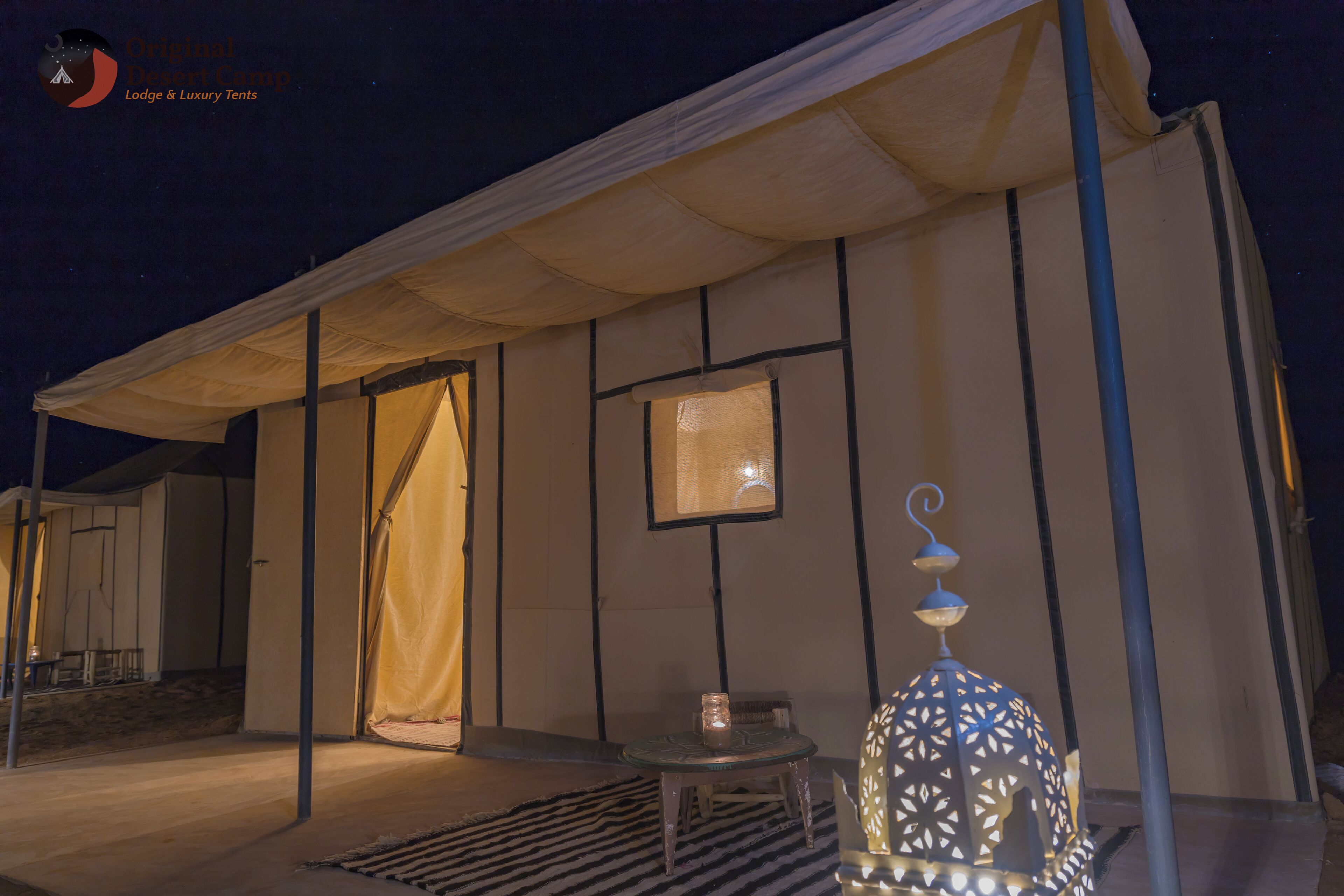 A tented accommodation with a covered outdoor seating area, a table with a candle, and a decorative lantern.