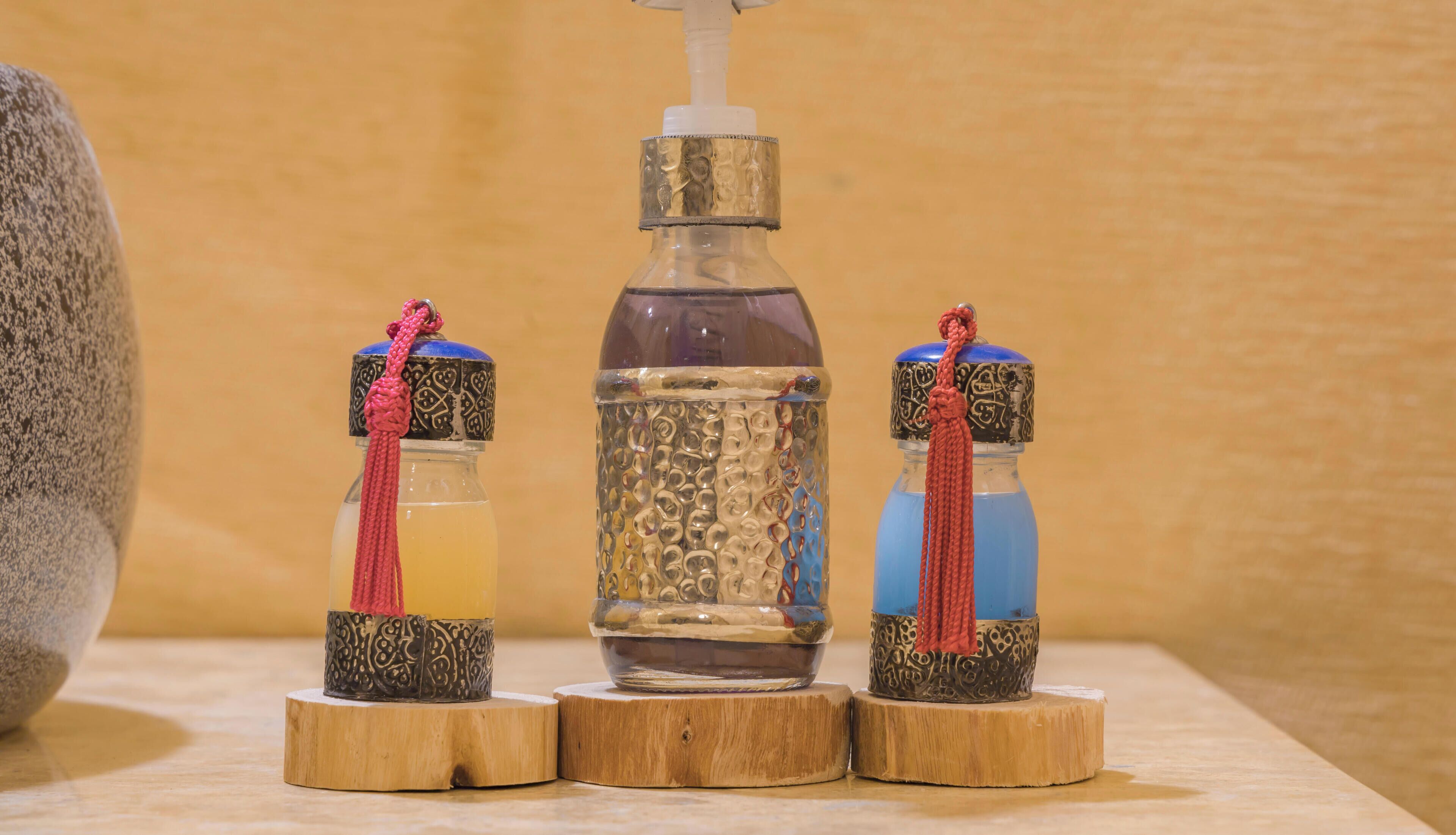 Drei Glasflaschen mit gemusterten Basen und roten Quasten, auf Holzständer gestellt.
