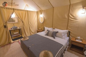 Un dormitorio tipo tienda de campaña con una cama, mesitas de noche, un espejo y una pequeña mesa con artículos de aseo.