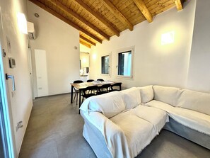 A modern interior with a wooden ceiling, a white sofa, a dining table with chairs, and two windows. - FilMa Seagarden Villa (Santa Margherita di Pula)
