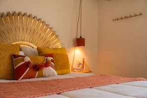 Una cama con cabecera dorada, varios almohadones y una manta roja, con una lámpara colgante.