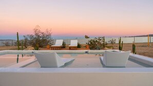 Un espace piscine avec des chaises longues et une vue sur la mer au coucher du soleil.