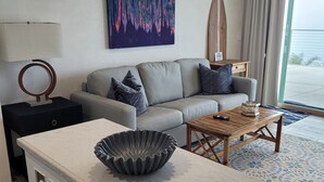 A modern living room with a grey sofa, a coffee table, a decorative bowl, a painting, and a view of the outdoors. - Ocean Sunsets 1 bd Guesthouse
Forever ocean views, short stroll to the sand  (Malibu)