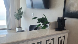 A modern living room with a white cabinet, a coffee maker, a TV, and two potted plants. - Ocean Sunsets 1 bd Guesthouse
Forever ocean views, short stroll to the sand  (Malibu)